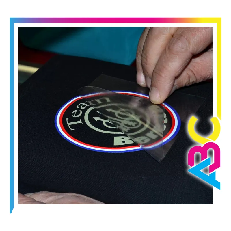 Flocage textile en cours sur un polo, réalisé par Atelier Brod’Art Créations à Soissons – retrait du film de transfert.