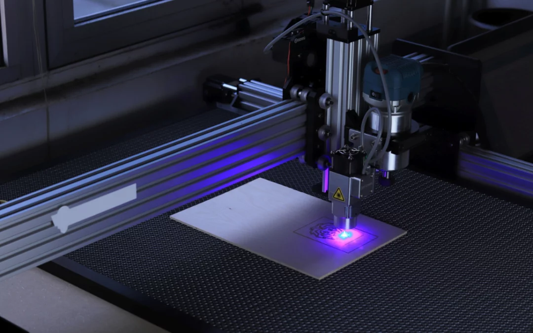 Machine de gravure laser en train de dessiner un motif sur bois avec faisceau lumineux bleu